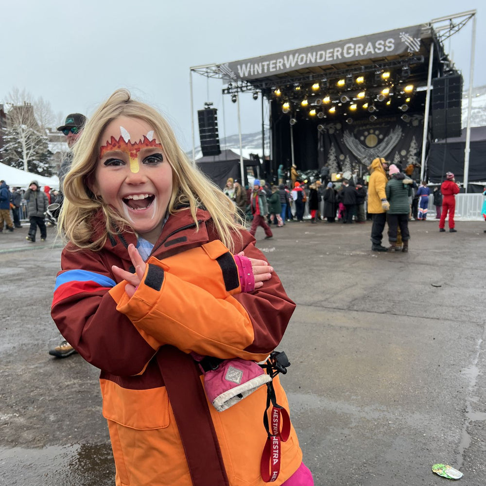 Girl in Town Hall warm jacket with dragon facepaint in front of Winter WonderGrass Stage.