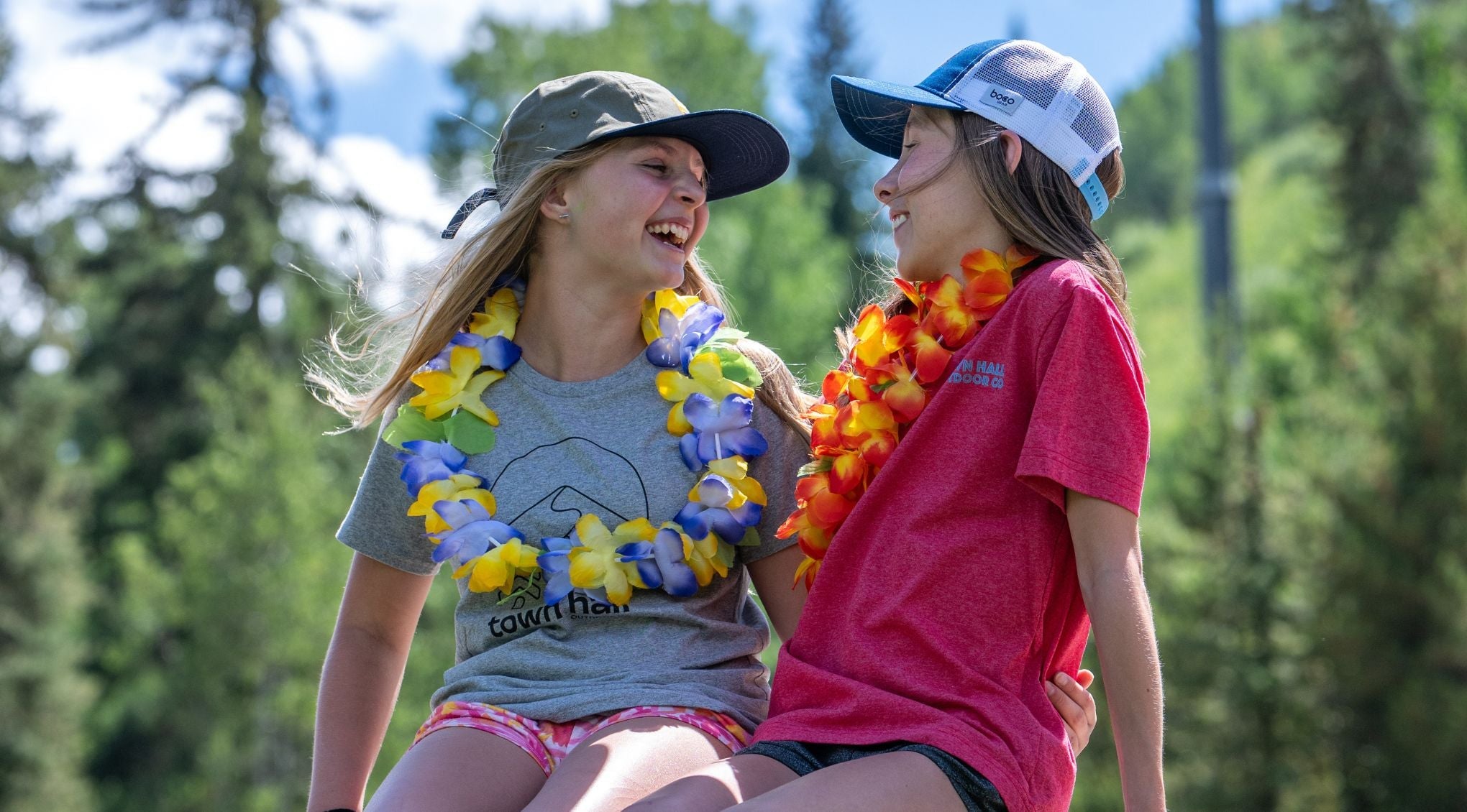 girls laughing wearing hats and tees on a bench in the woods