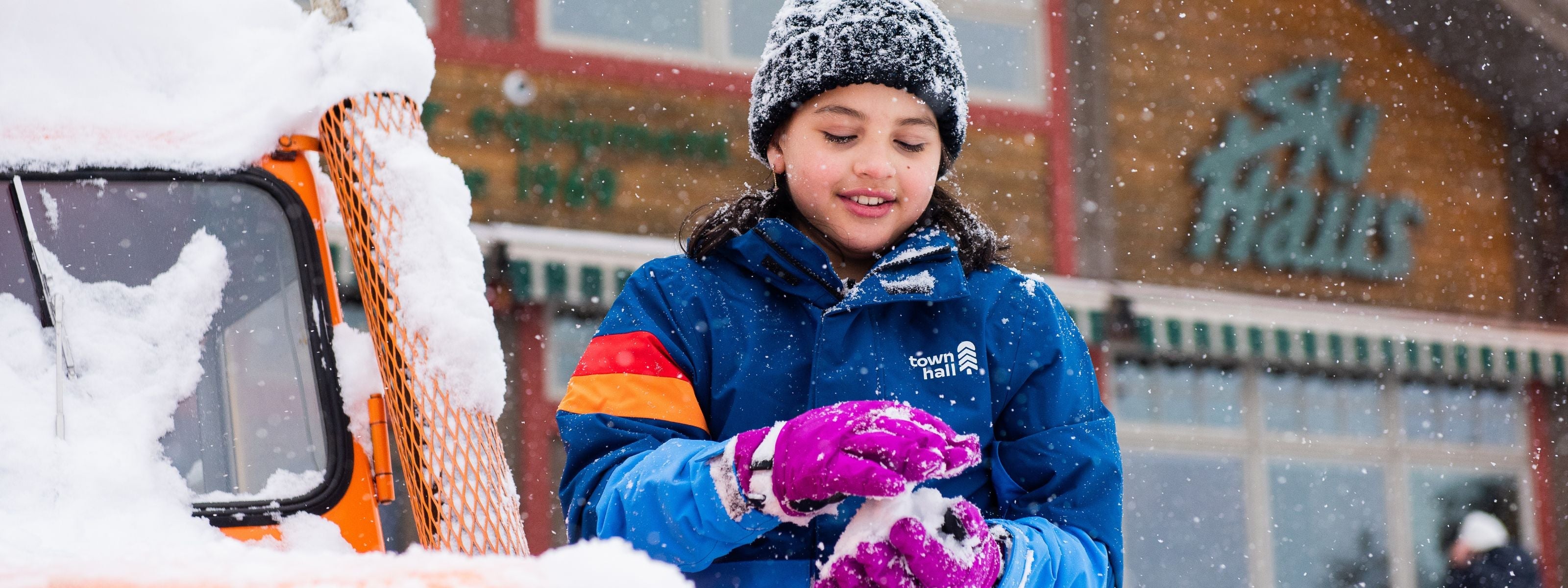 girl making snowball in colorful jacket while snow falls