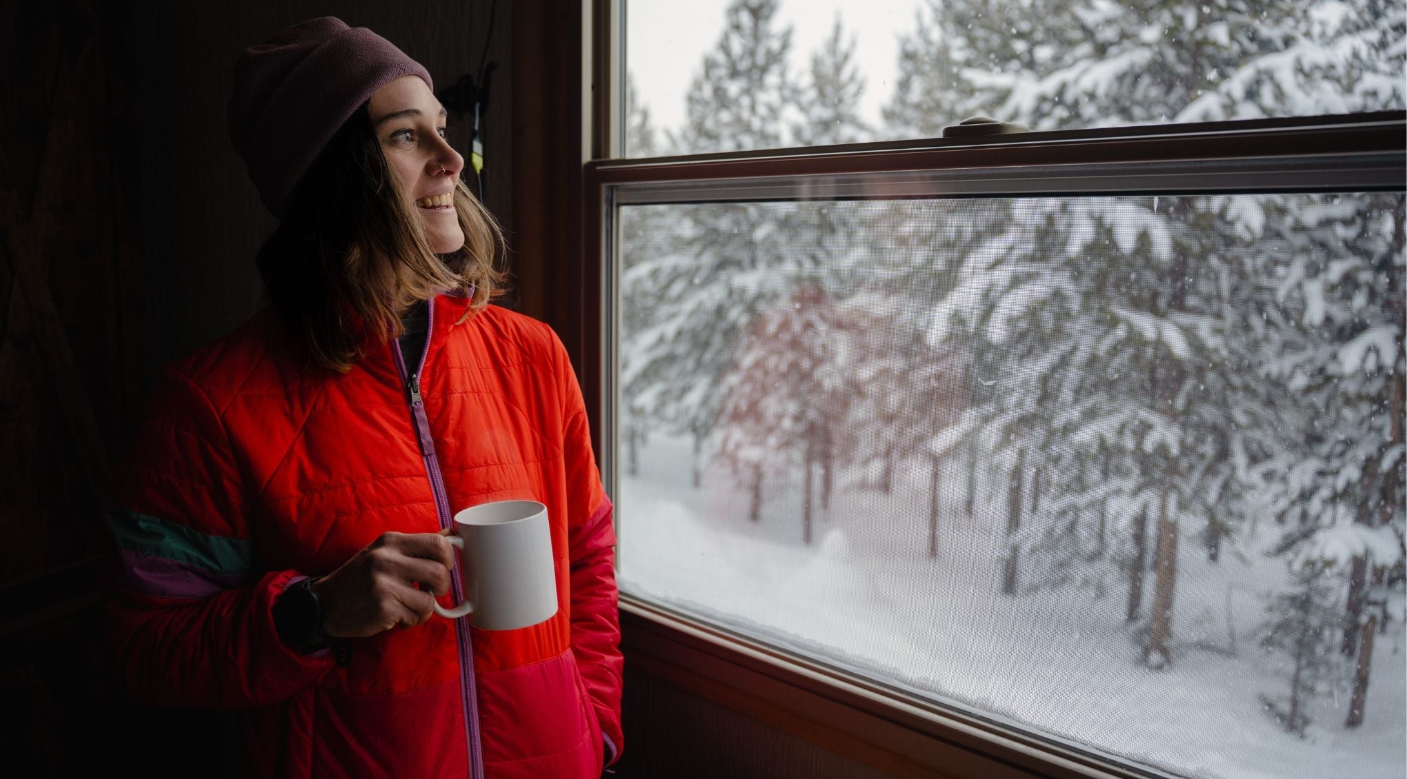 mom looking out window of hut and into snow wearing jacket