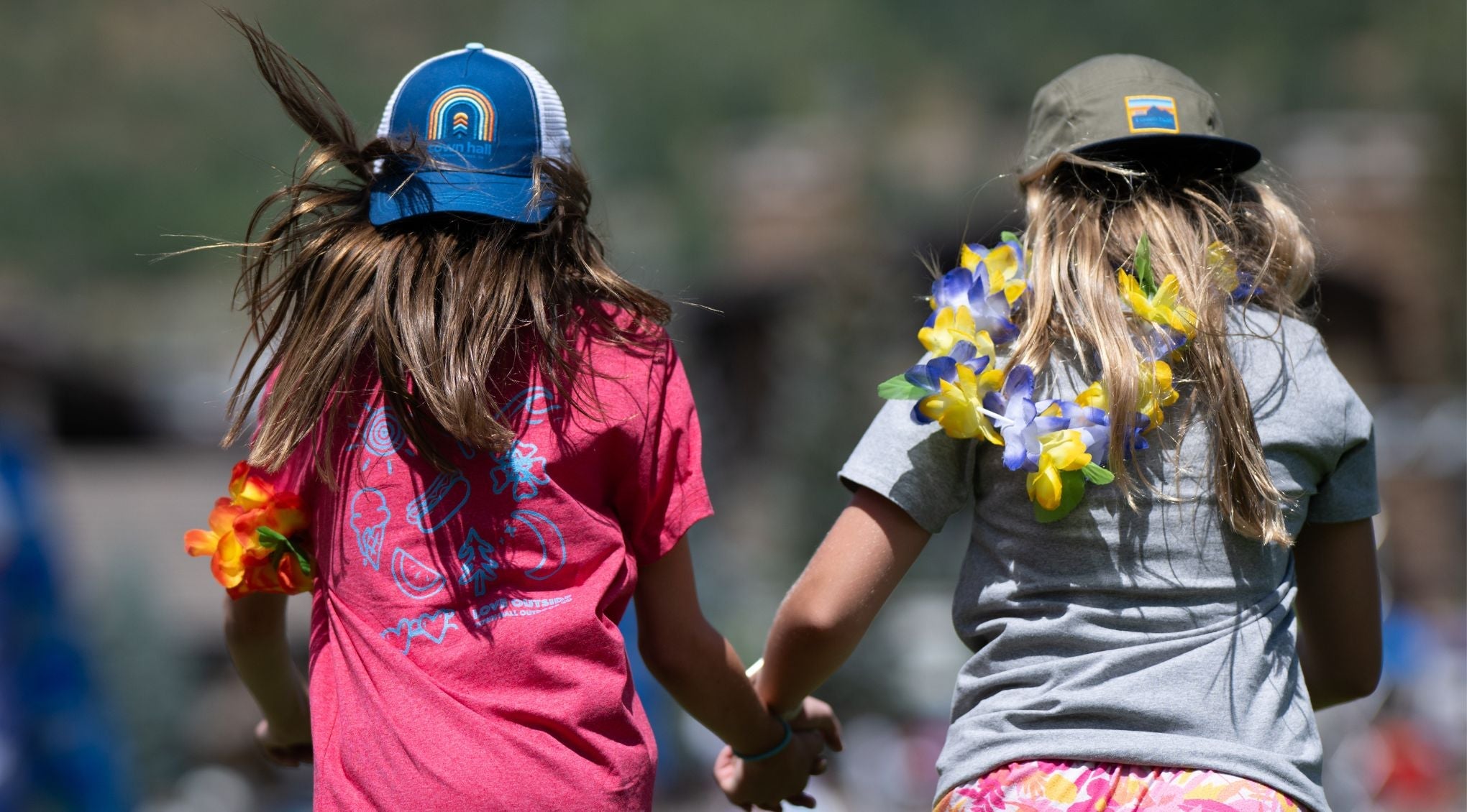 Girls holding hands skipping in hats and tee shirts