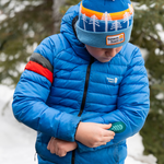 Child exploring outdoors in a blue jacket featuring a bright pine NOSO Gear Repair Patch, demonstrating how kids' favorite adventure gear can get a second life.