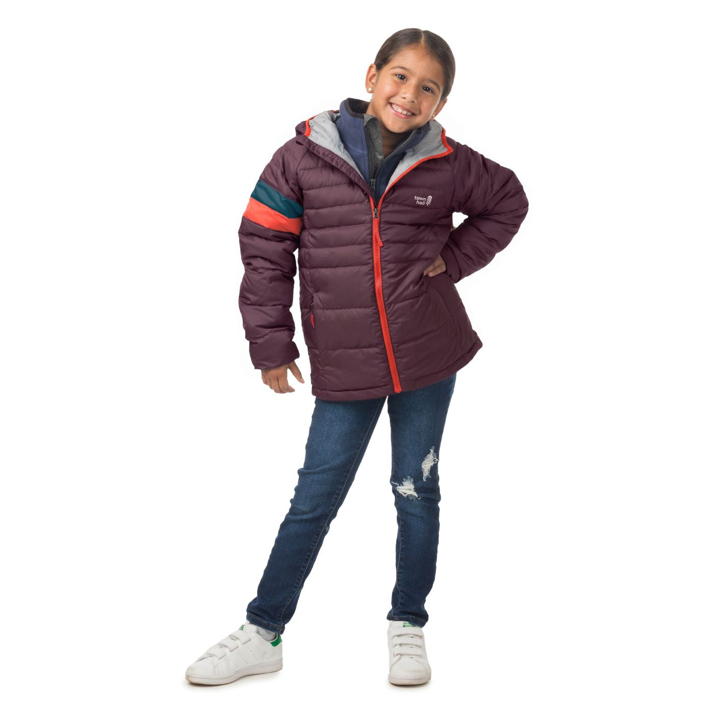 A young girl modeling a dark purple puffer jacket with orange and teal stripes on the sleeve, blue jeans, and white sneakers against a white background.