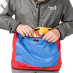 Boy demonstrating the About Town Anorak's built-in stuff sack pouch feature, perfect for packing away when weather clears during hiking or biking adventures.
