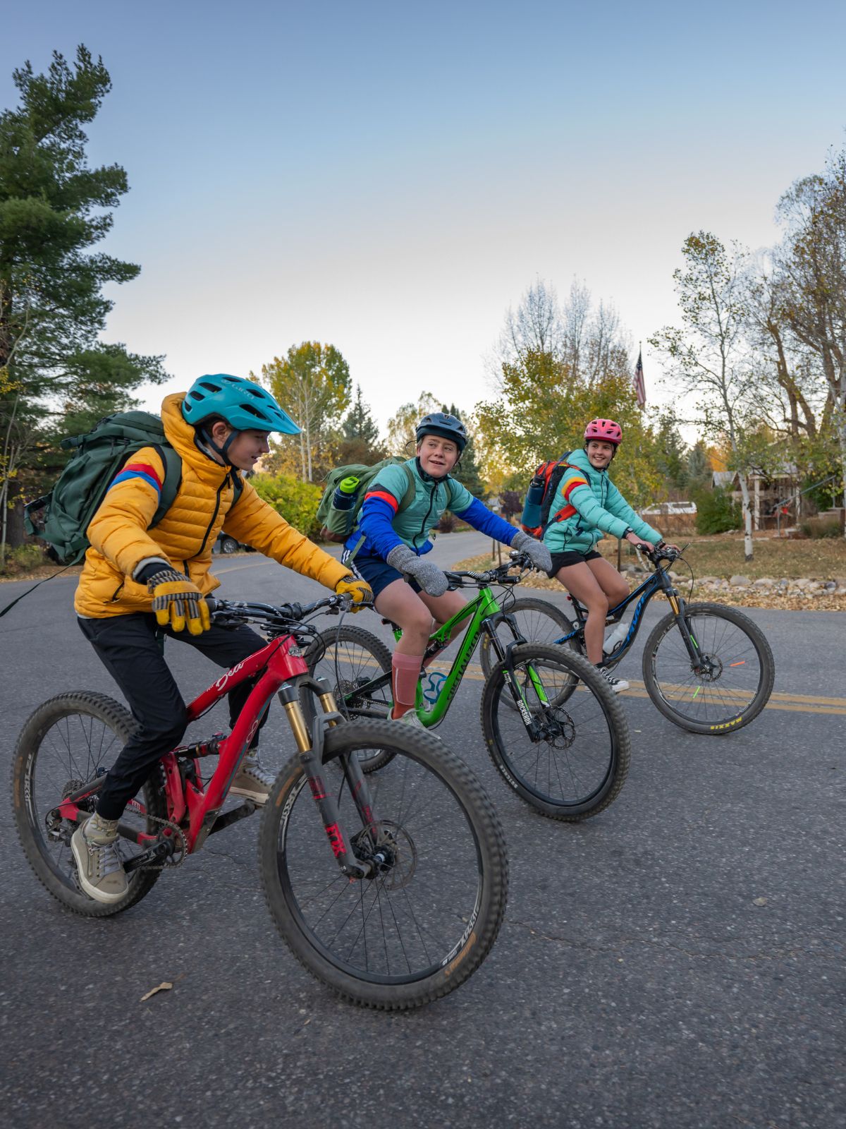 three kids on mountain bikes riding to school wearing colorful, warm jackets