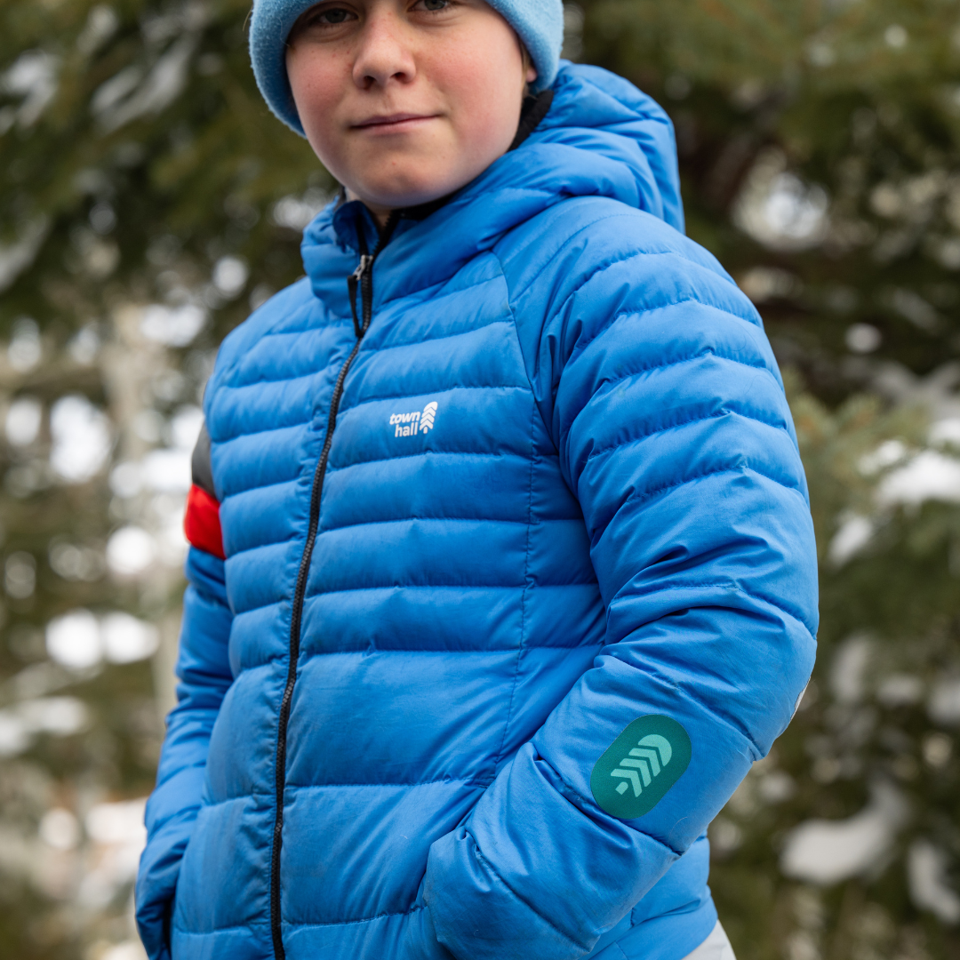 Close-up of a child's blue jacket sleeve featuring a bright pine NOSO Gear Repair Patch, showing how these easy-to-apply patches keep kids' gear adventure-ready.