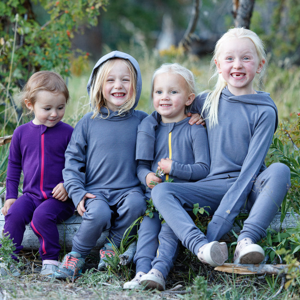 PRIZE ONE: Adventure Jogger Set (Kids) Your choice of color and size, for kids age 2-14. Retail Value  $198 PRIZE TWO: Merino Adventure Hoodie. Four kids sitting outside camping and wearing merino baselayers and smiling.