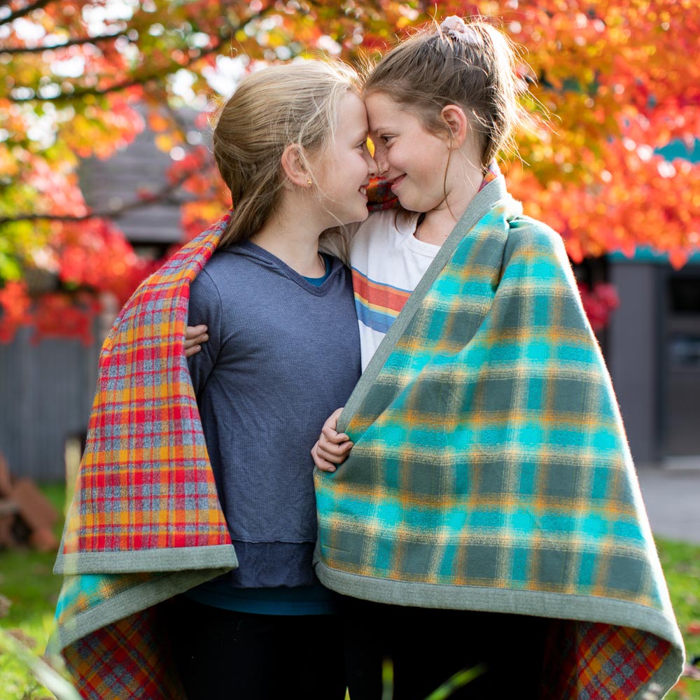 Kids in the fall leaves, outside holding a cozy blanket and enjoying being together. 