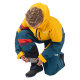 Child adjusting the gray ankle gaiter over a boot while wearing a Blue Coral Mountain Town kids snow bib.