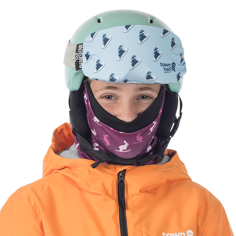 Person wearing a helmet with a patterned cover and an orange jacket on a white background