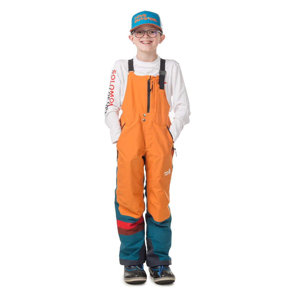Child wearing Town Hall's Peach Caramel/Blue Coral Mountain Town Winter Bib, made for keeping little adventurers warm and dry during backyard sledding sessions.