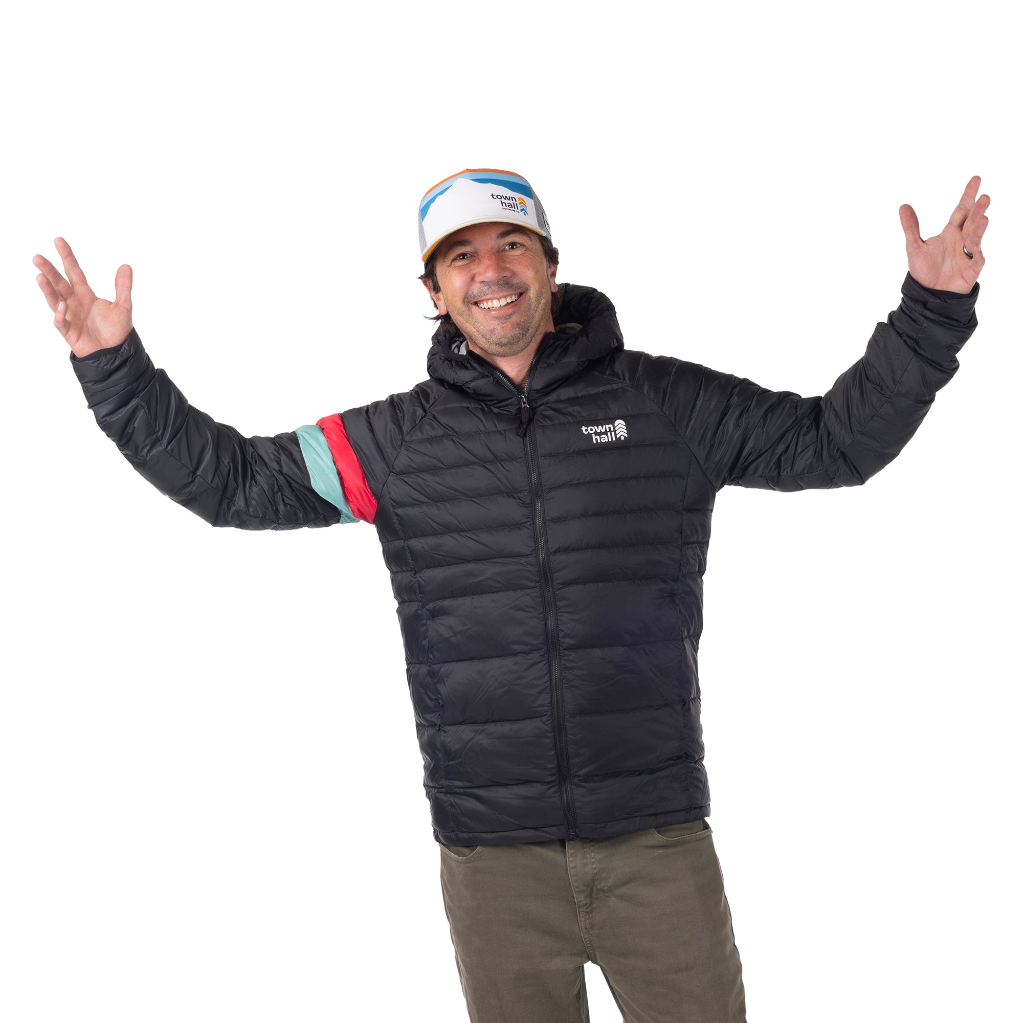 Smiling man wearing the mountain-print Town Hall Trucker Hat and a black puffy jacket with arms raised.