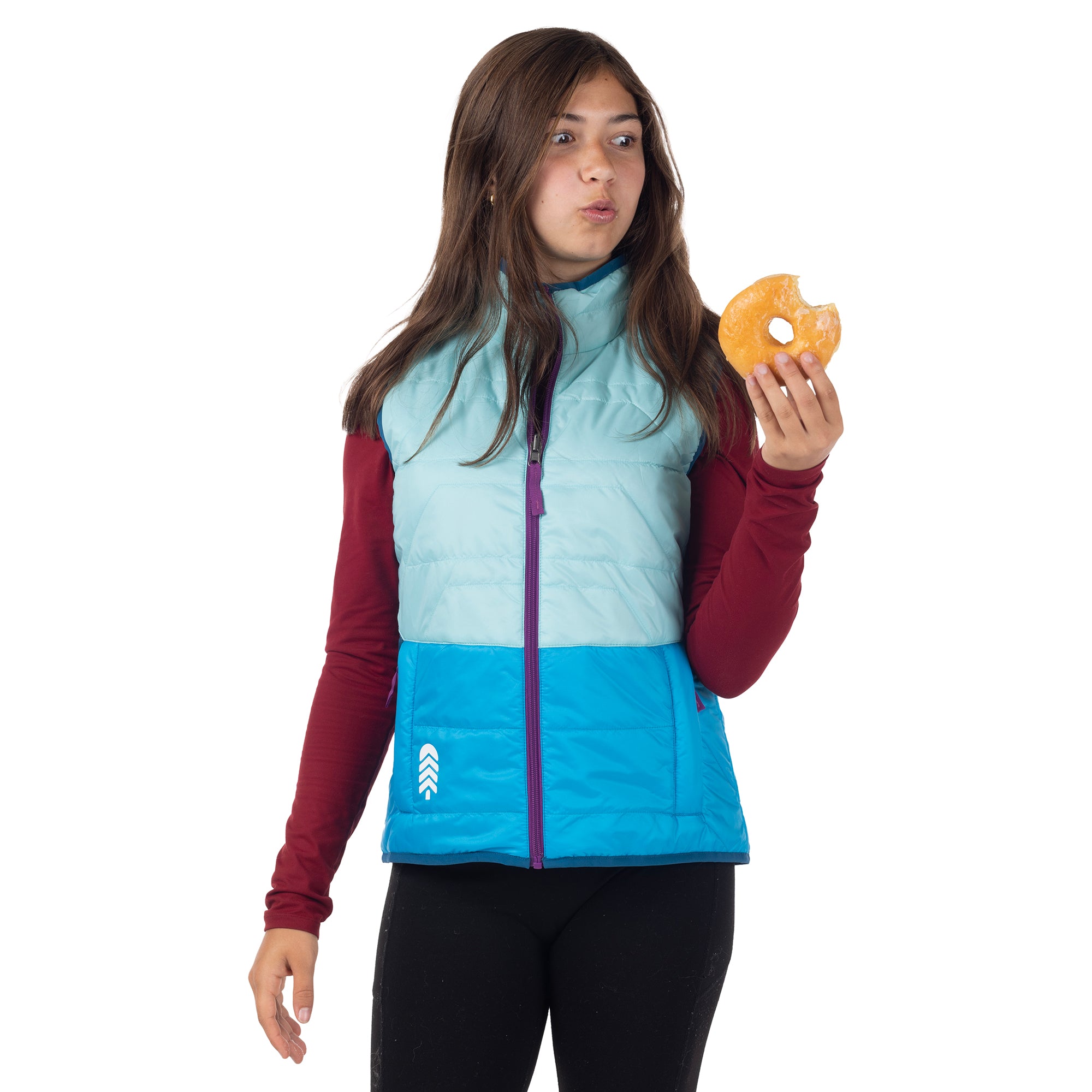 Girl eating a donut in a blue puffy vest and smiling with excitement.