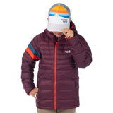 Model tipping the brim of the mountain-print Town Hall Trucker Hat while wearing a purple puffy jacket.