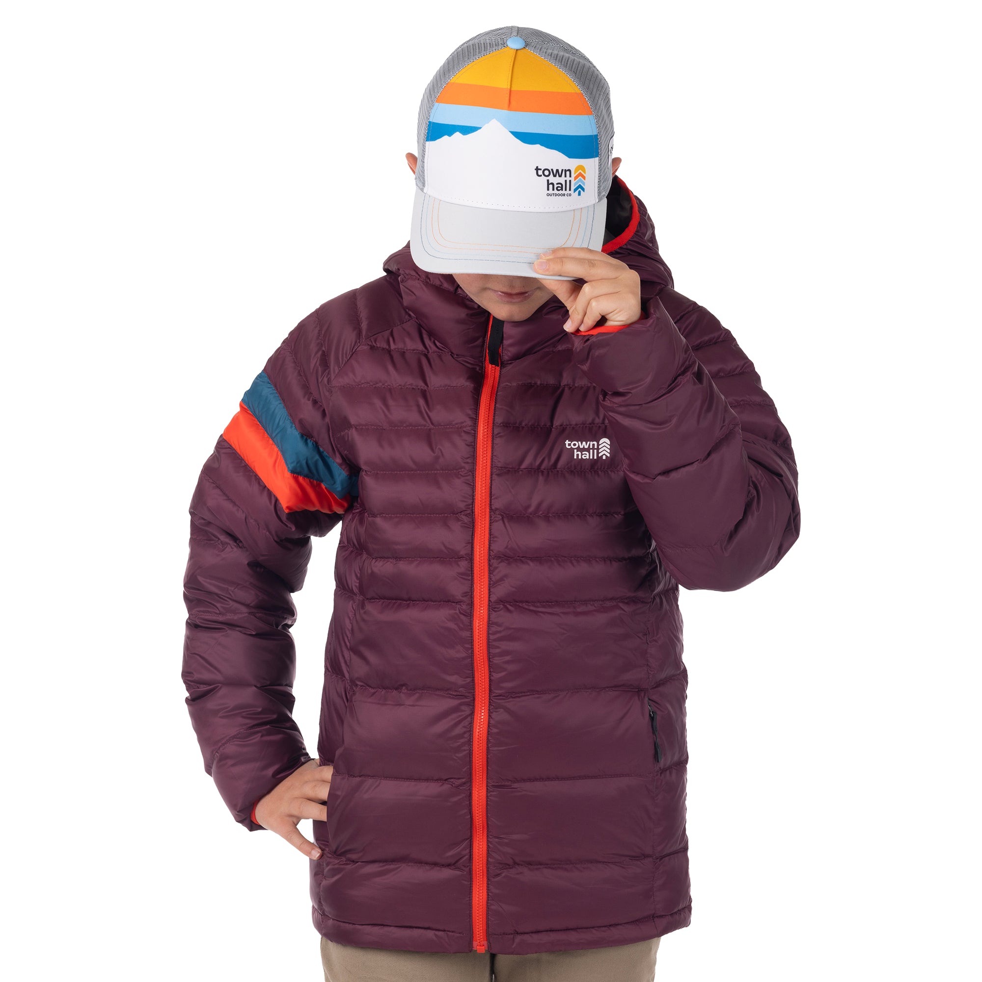 Model tipping the brim of the mountain-print Town Hall Trucker Hat while wearing a purple puffy jacket.
