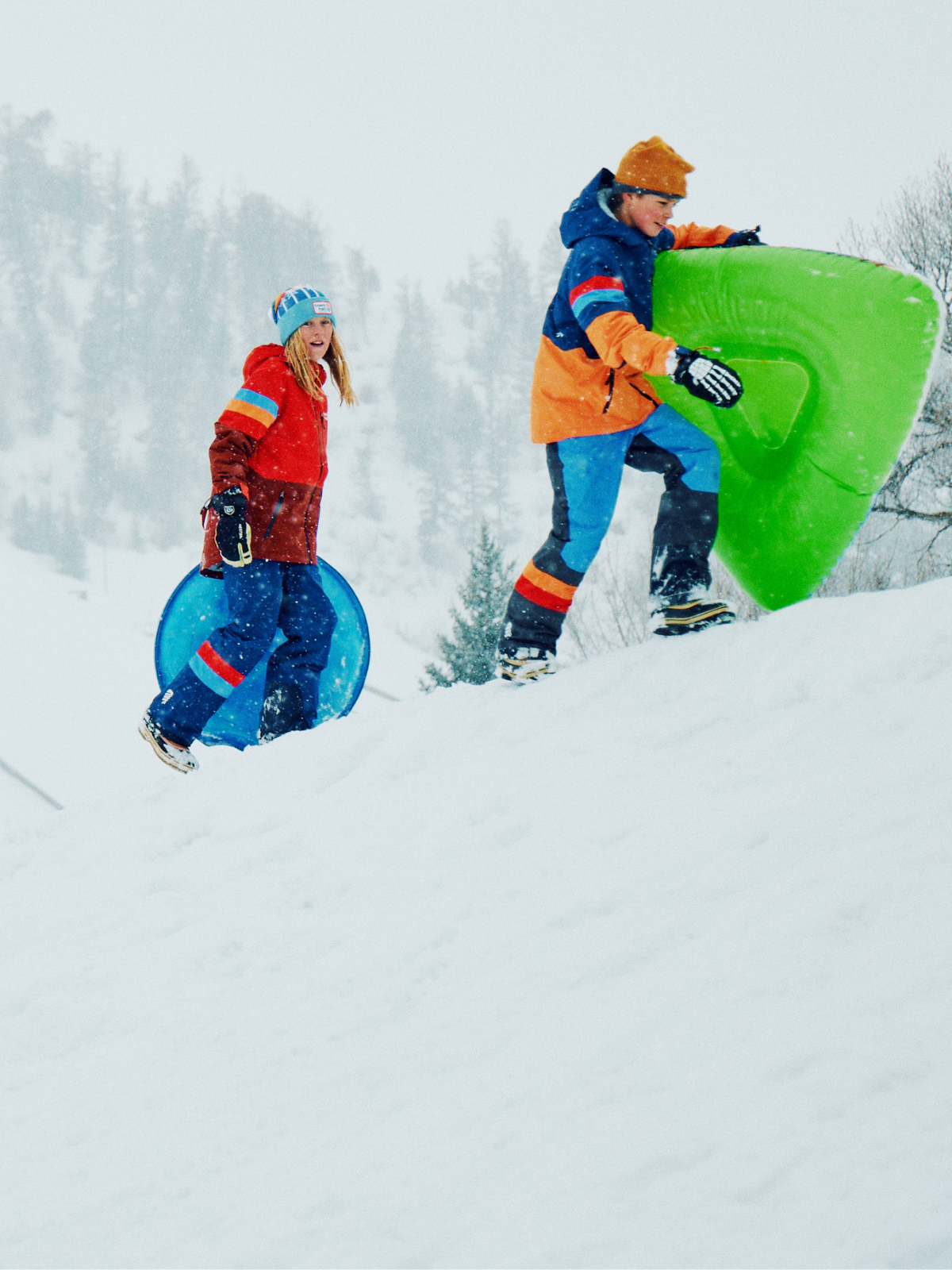 Two children with colorful sleds in a snowy landscape