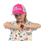 Child wearing a pink Town Hall Kids Trucker Hat with Love Outside lettering, making a heart with their hands.