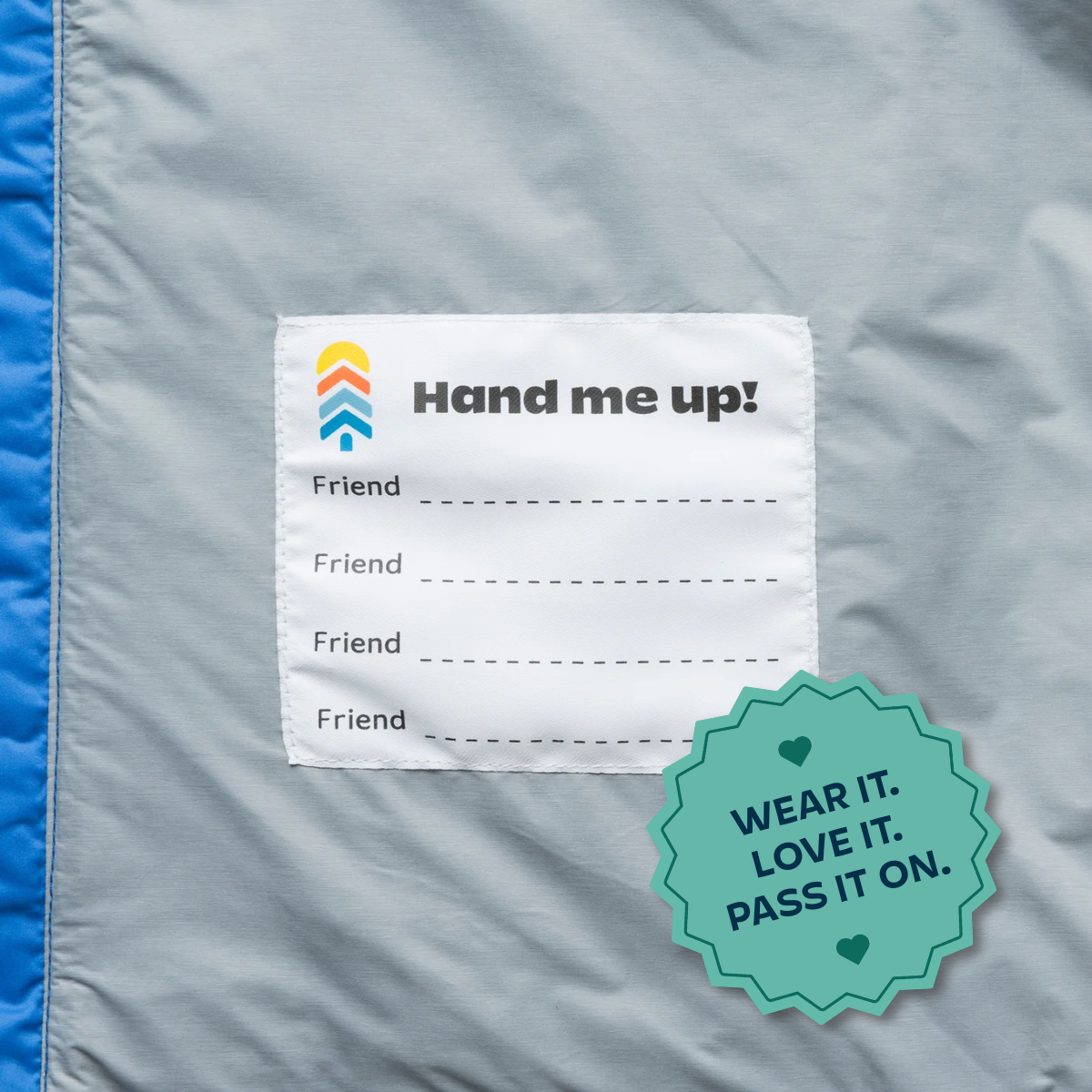 Label on a jacket with 'Hand me up!' branding and a tagline, on a gray fabric background.