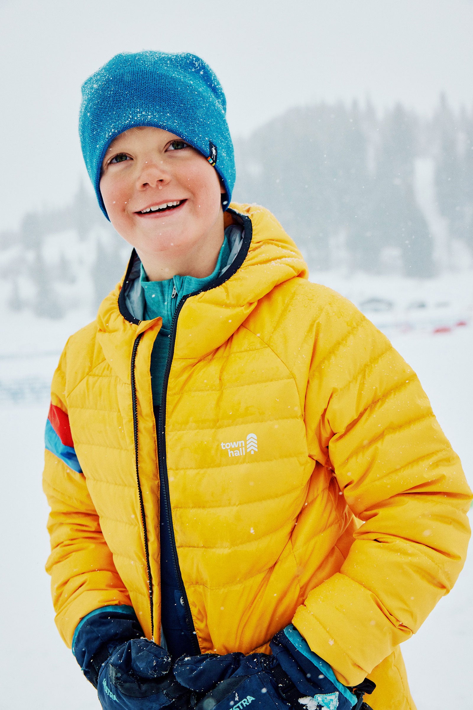 Child wearing a yellow jacket and blue beanie in a snowy landscape