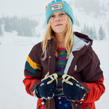 A young girl wearing a turquoise Town Hall beanie, a dark brown and red ski jacket, and dark blue gloves, standing in a snowy outdoor setting.