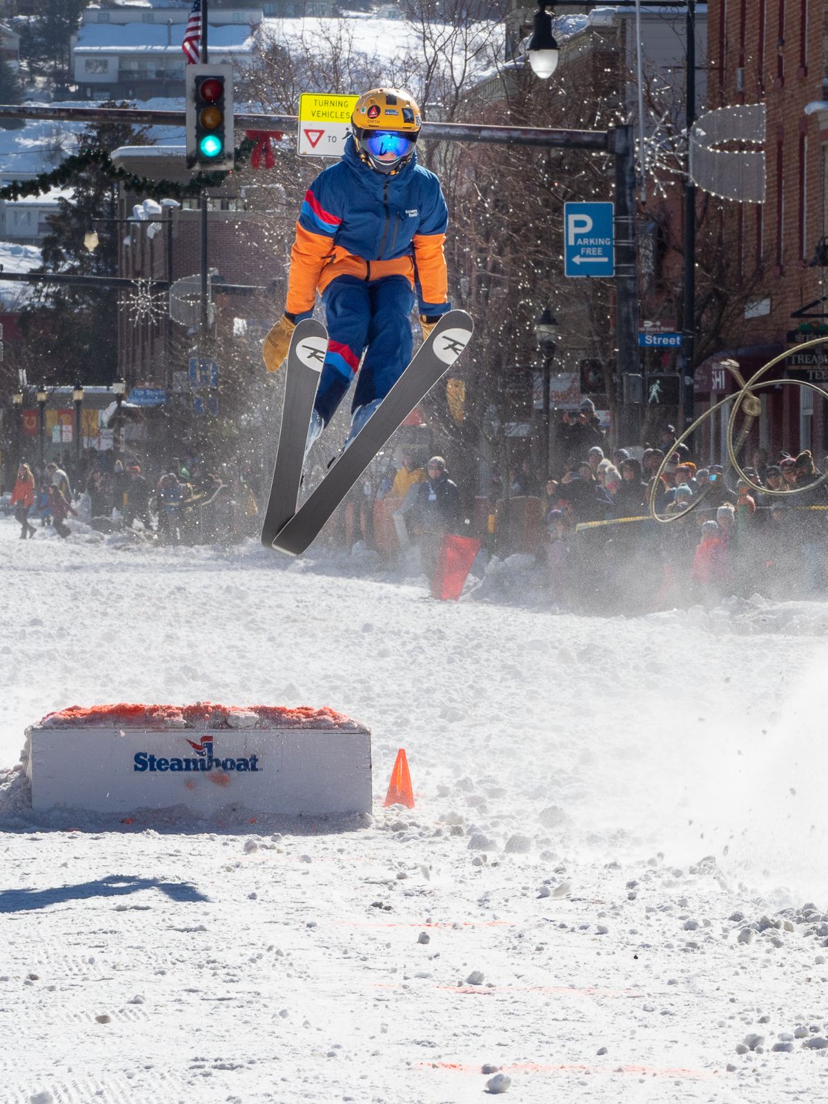 Person skiing off a ramp with Steamboat Springs branding in a snowy urban setting.